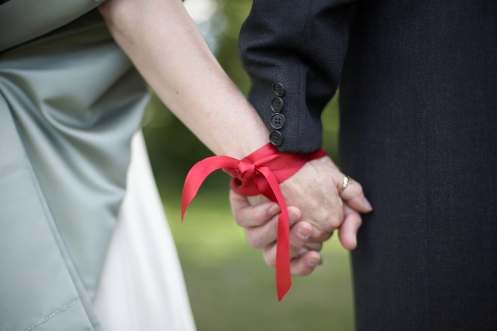 Man and woman holding hands, their wrists tied together with a ribbon