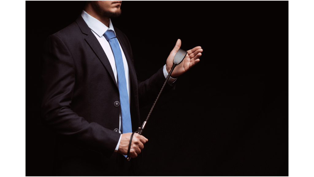 Man in a suit resting a riding crop against his palm