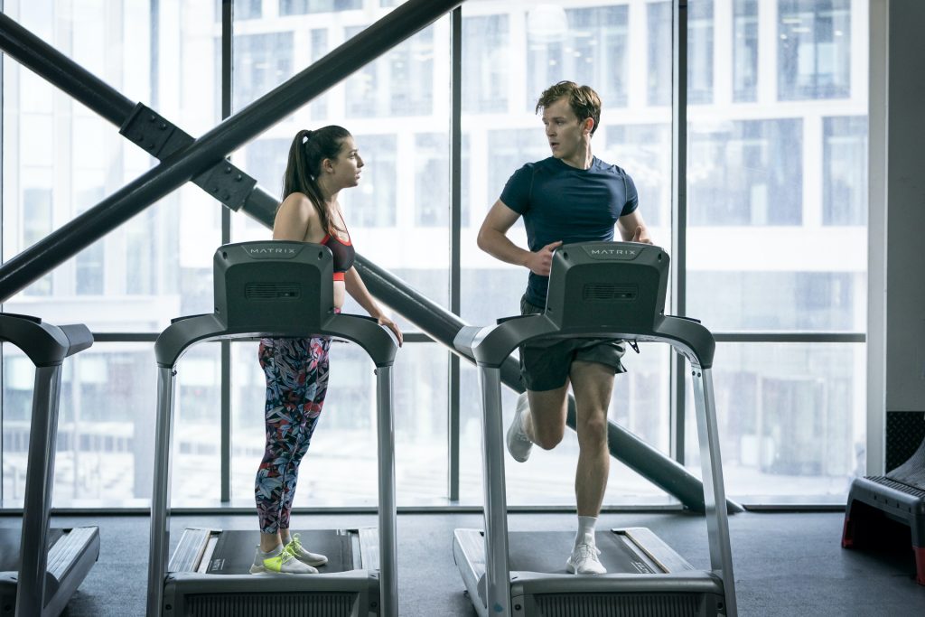 Yasmin and Robert from Industry looking at each other as she stands still on a treadmill and he runs on the one next to her.
