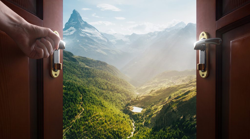 Doors opening to a dramatic view of a lush valley with mountains in the background.