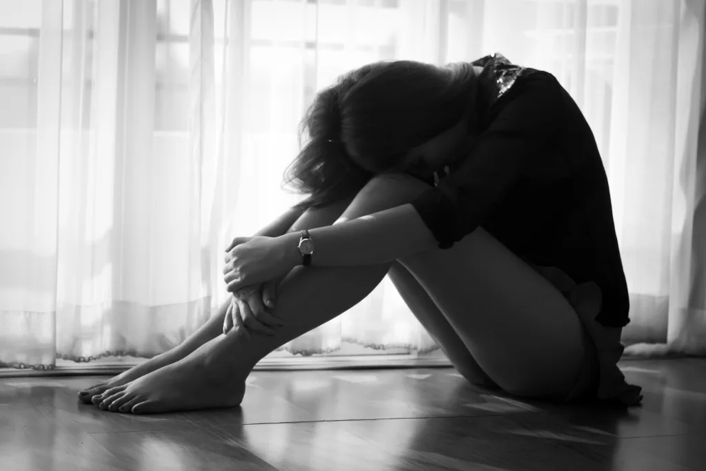 Woman sitting on floor with her head bent on her knees.