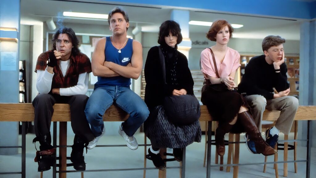 Scene from The Breakfast Club of a group of teens sitting in a row sullenly.