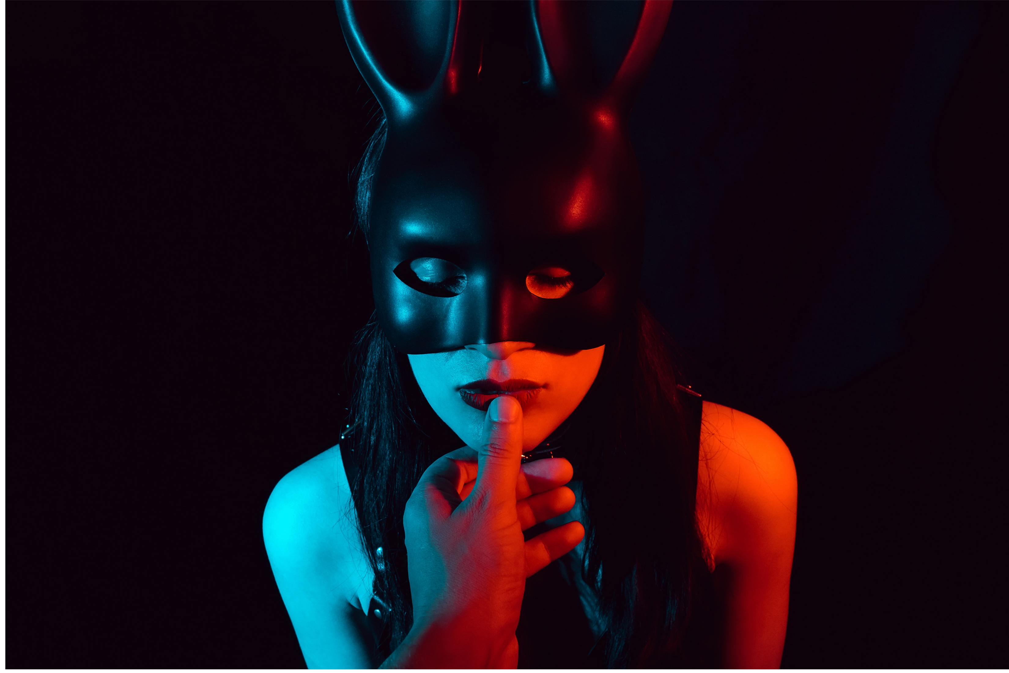 Woman wearing black mask covering the top of her face. A man's thumb is on her mouth.