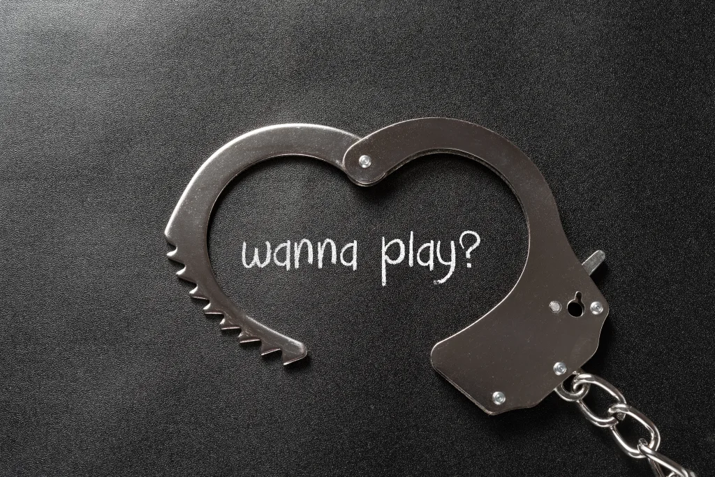 Open handcuffs with the text "wanna play?" written in the middle